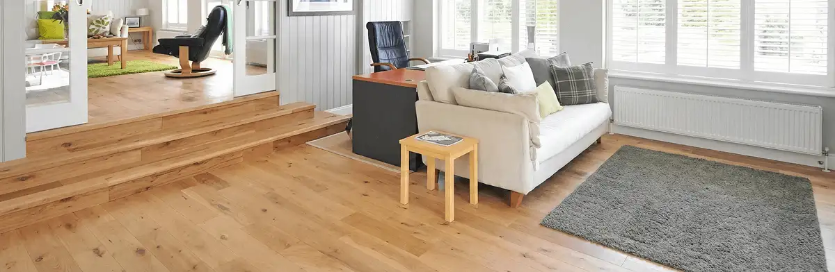 A modern living room with professionally installed laminate flooring, a beige sofa, a small side table, a gray rug, and large windows with white shutters in Boca Raton, FL